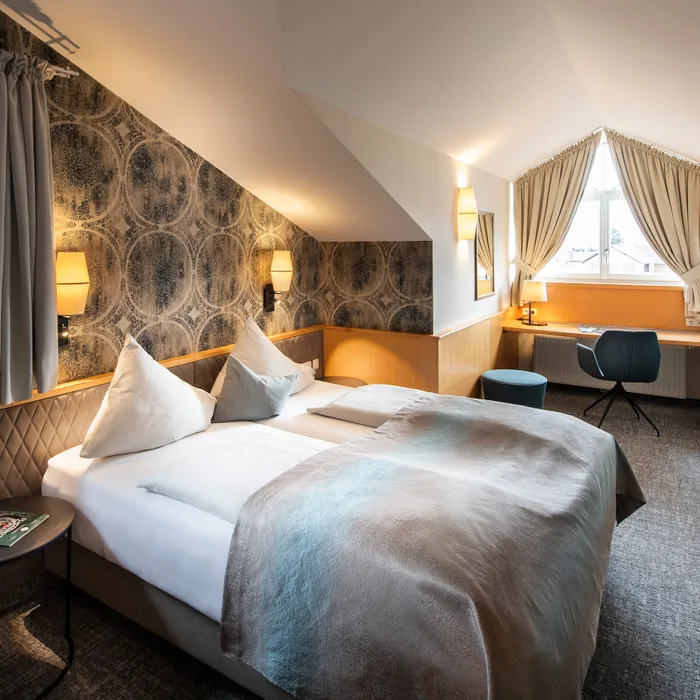 Camera d'hotel moderna con letto matrimoniale, soffitto inclinato, scrivania vicino alla finestra e TV a parete
